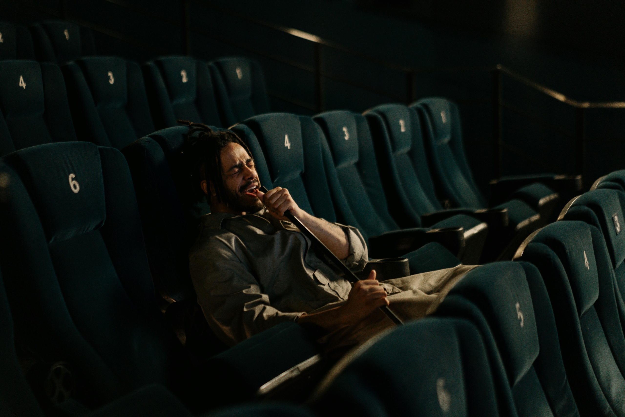 A man singing passionately in an empty cinema, microphone in hand.